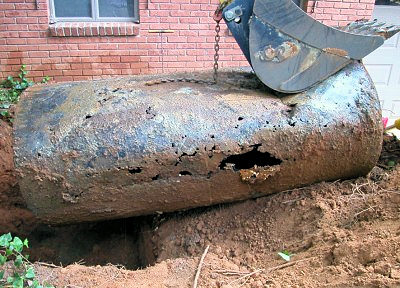 Severely corroded underground oil tank being removed from the ground.